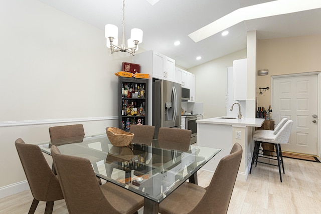 dining area featuring vaulted ceiling with skylight, an inviting chandelier, light hardwood / wood-style flooring, and sink