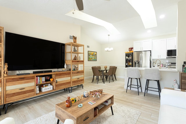 living room featuring ceiling fan with notable chandelier, light wood-type flooring, sink, and vaulted ceiling