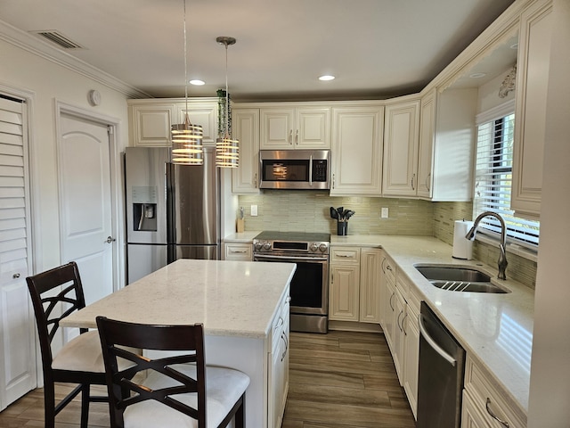 kitchen with a kitchen bar, stainless steel appliances, sink, a center island, and hanging light fixtures