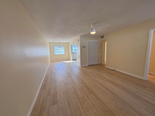 empty room with ceiling fan with notable chandelier and light wood-type flooring