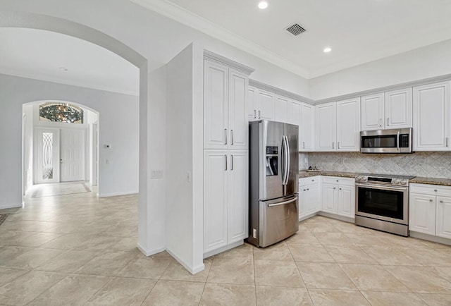 kitchen with stainless steel appliances, light tile patterned floors, tasteful backsplash, white cabinets, and ornamental molding