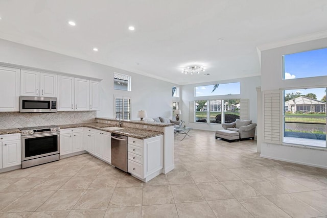 kitchen with kitchen peninsula, appliances with stainless steel finishes, white cabinets, and light stone counters