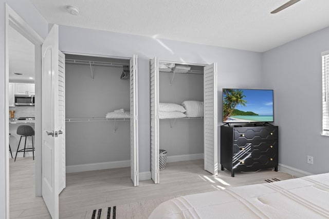 bedroom featuring ceiling fan, light wood-type flooring, and multiple closets