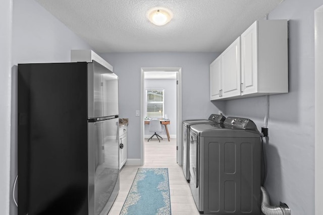 washroom featuring washing machine and clothes dryer, cabinets, a textured ceiling, and light wood-type flooring