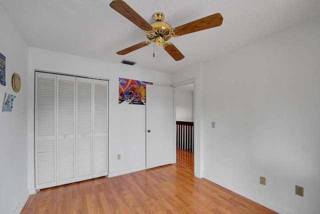 unfurnished bedroom featuring a textured ceiling, a closet, light hardwood / wood-style flooring, and ceiling fan