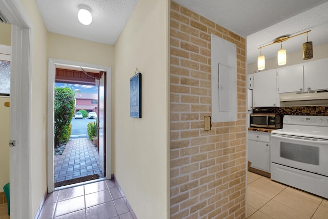 kitchen featuring hanging light fixtures, white electric range oven, white cabinets, brick wall, and light tile patterned flooring