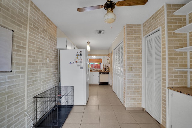 kitchen featuring white appliances, ceiling fan, light tile patterned floors, white cabinetry, and brick wall