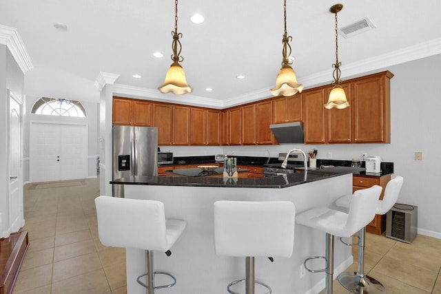 kitchen featuring hanging light fixtures, stainless steel appliances, a kitchen breakfast bar, an island with sink, and ornamental molding