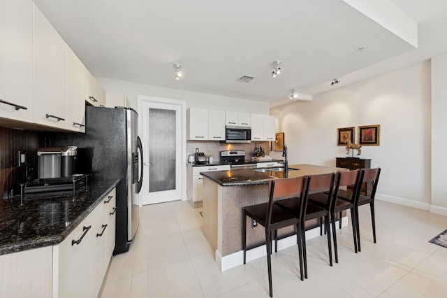 kitchen featuring backsplash, stainless steel appliances, a kitchen island with sink, sink, and white cabinets