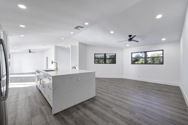 kitchen with light stone countertops, dark wood-type flooring, sink, white cabinetry, and an island with sink