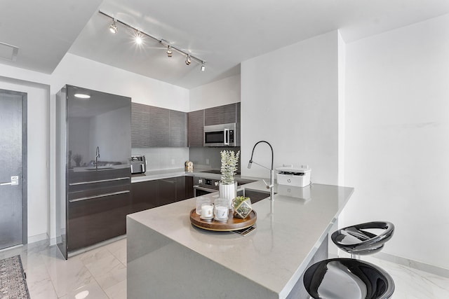 kitchen featuring sink, kitchen peninsula, track lighting, a breakfast bar, and dark brown cabinets