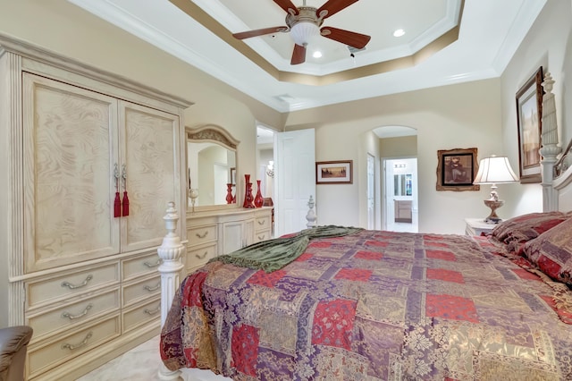 bedroom with a tray ceiling, ensuite bath, ceiling fan, and crown molding