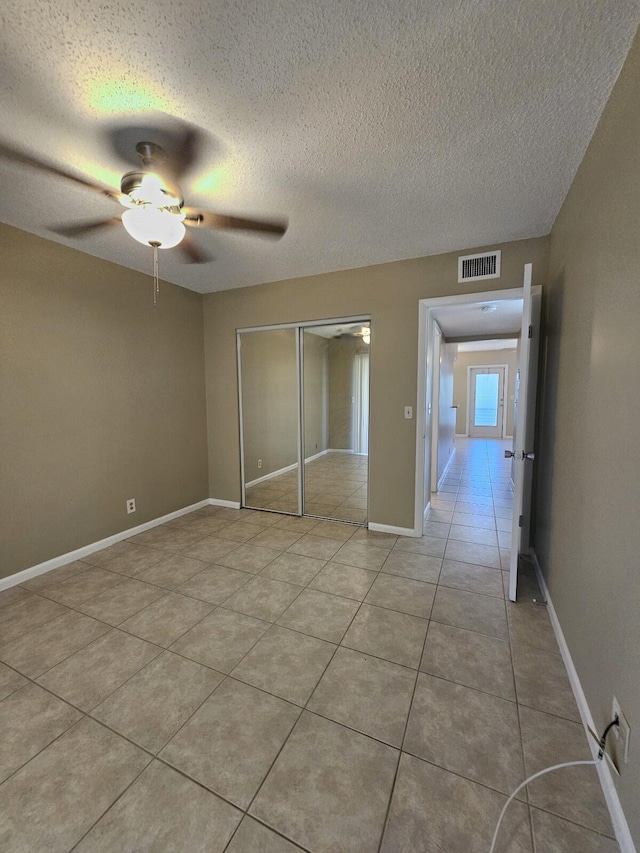 unfurnished bedroom featuring ceiling fan, a closet, light tile patterned flooring, and a textured ceiling