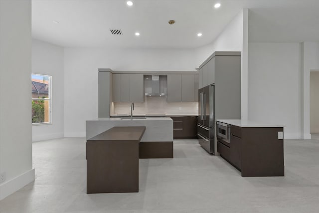 kitchen featuring decorative backsplash, a kitchen island with sink, stainless steel appliances, and wall chimney range hood