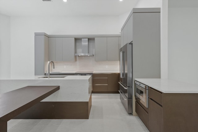 kitchen with gray cabinetry, backsplash, sink, wall chimney exhaust hood, and stainless steel appliances