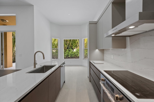 kitchen with light stone countertops, appliances with stainless steel finishes, backsplash, sink, and wall chimney range hood