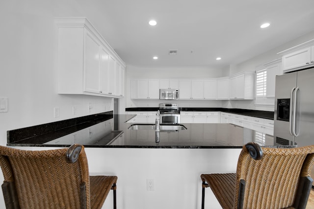 kitchen with white cabinets, appliances with stainless steel finishes, kitchen peninsula, and a breakfast bar area