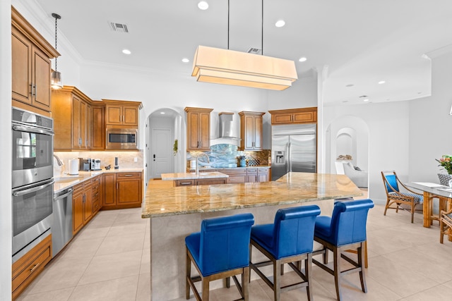 kitchen featuring built in appliances, decorative light fixtures, wall chimney exhaust hood, and a spacious island