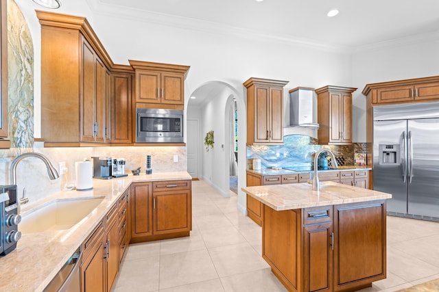 kitchen featuring sink, wall chimney range hood, built in appliances, a kitchen island, and ornamental molding