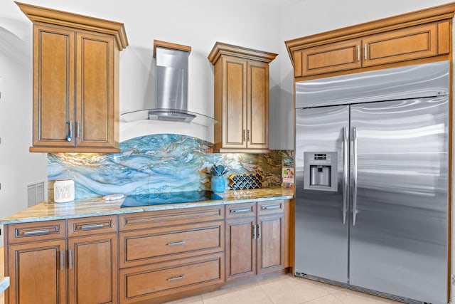 kitchen featuring wall chimney range hood, built in refrigerator, black electric cooktop, light tile patterned floors, and tasteful backsplash