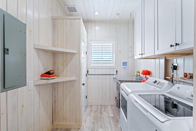 washroom featuring washer and clothes dryer, cabinets, light wood-type flooring, and wooden walls