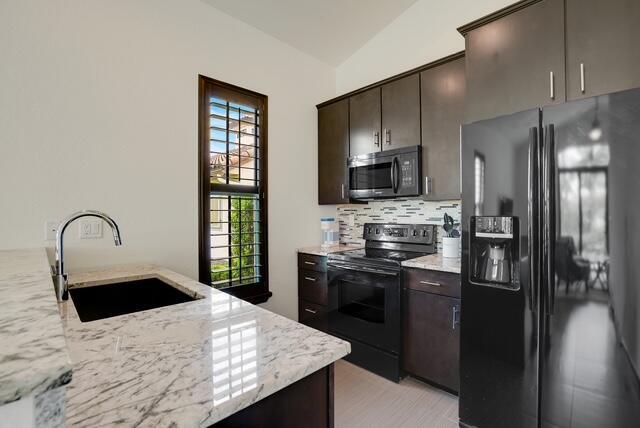 kitchen with backsplash, dark brown cabinets, sink, black appliances, and lofted ceiling