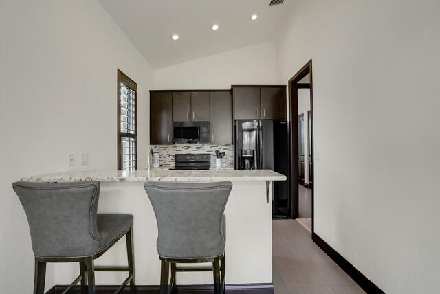 kitchen featuring dark brown cabinetry, a kitchen breakfast bar, kitchen peninsula, lofted ceiling, and black appliances