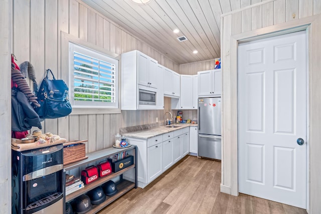 kitchen with stainless steel appliances, sink, white cabinets, light hardwood / wood-style floors, and wood walls