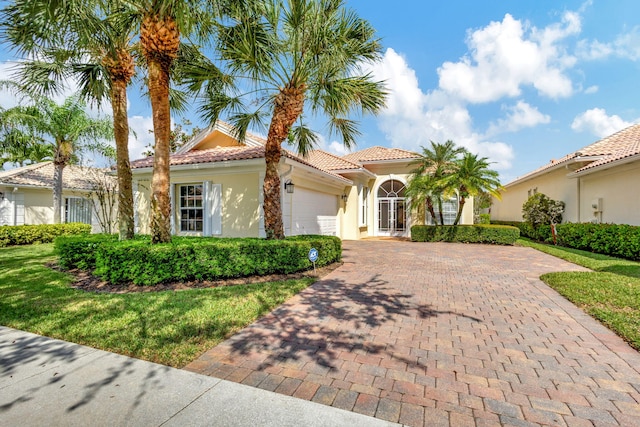 mediterranean / spanish home with decorative driveway, a tile roof, an attached garage, and stucco siding