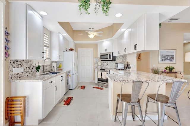 kitchen with sink, light stone counters, kitchen peninsula, stainless steel appliances, and white cabinets