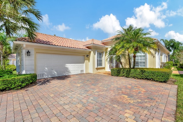 mediterranean / spanish-style house with a garage, decorative driveway, a tile roof, and stucco siding