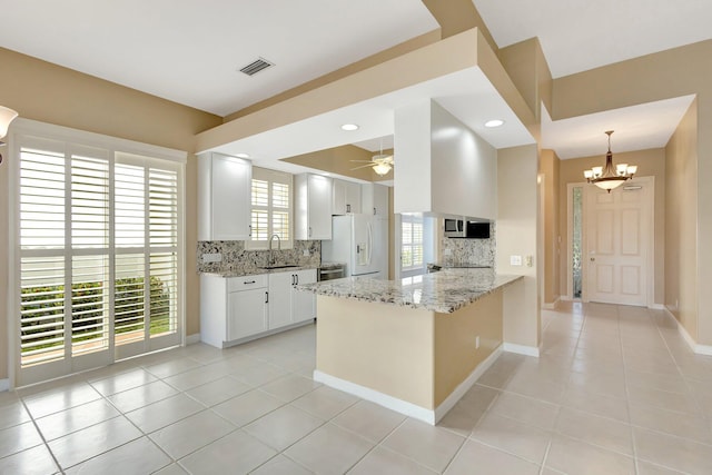 kitchen featuring white refrigerator with ice dispenser, visible vents, white cabinets, a peninsula, and light stone countertops