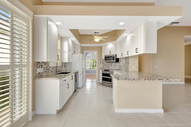 kitchen featuring a peninsula, a sink, white cabinetry, appliances with stainless steel finishes, and light stone countertops