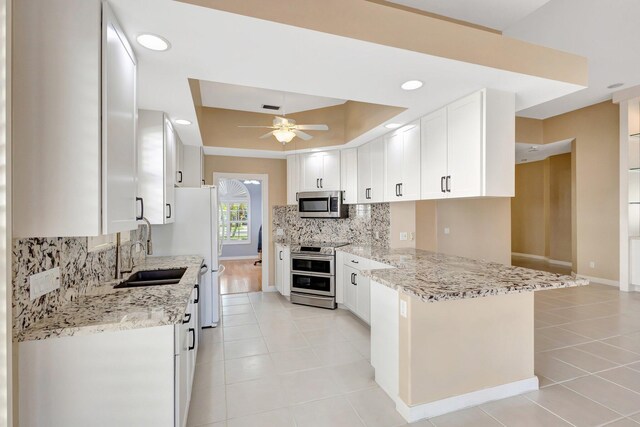 kitchen with stainless steel appliances, a peninsula, a sink, white cabinetry, and a raised ceiling