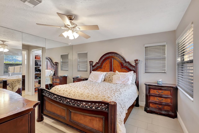 bedroom featuring ceiling fan, a closet, light tile patterned floors, and a textured ceiling