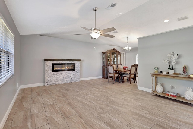 living room featuring ceiling fan with notable chandelier, a stone fireplace, plenty of natural light, and lofted ceiling