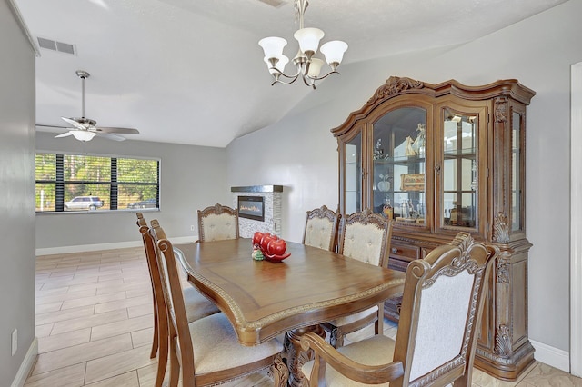 dining space featuring vaulted ceiling, a fireplace, and ceiling fan with notable chandelier