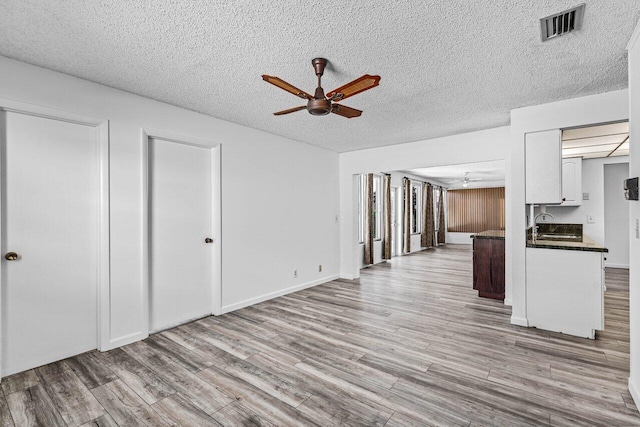 unfurnished living room with a textured ceiling, light hardwood / wood-style flooring, and ceiling fan