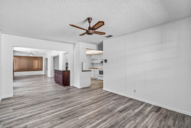 unfurnished living room featuring wooden walls, light hardwood / wood-style flooring, and ceiling fan