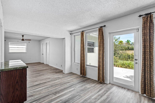 unfurnished living room with ceiling fan, light hardwood / wood-style flooring, a healthy amount of sunlight, and a textured ceiling