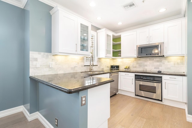 kitchen with sink, stainless steel appliances, backsplash, white cabinets, and light wood-type flooring