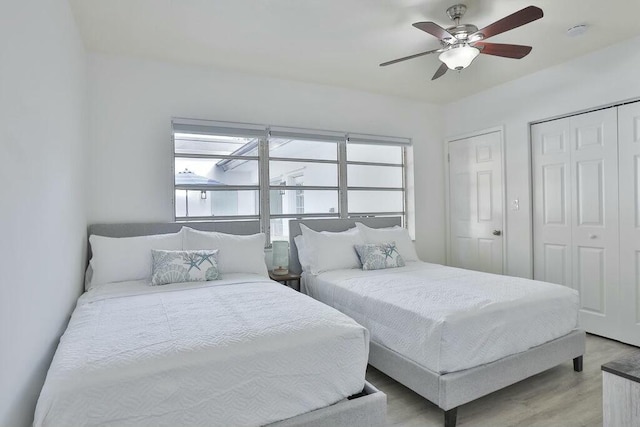 bedroom with two closets, light hardwood / wood-style floors, and ceiling fan