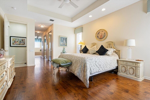 bedroom featuring ceiling fan, a raised ceiling, dark wood-type flooring, and multiple windows