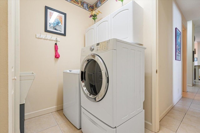 laundry room featuring washing machine and dryer, light tile patterned floors, and cabinets