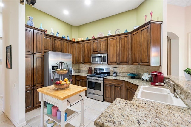 kitchen featuring light stone countertops, sink, stainless steel appliances, decorative backsplash, and light tile patterned floors