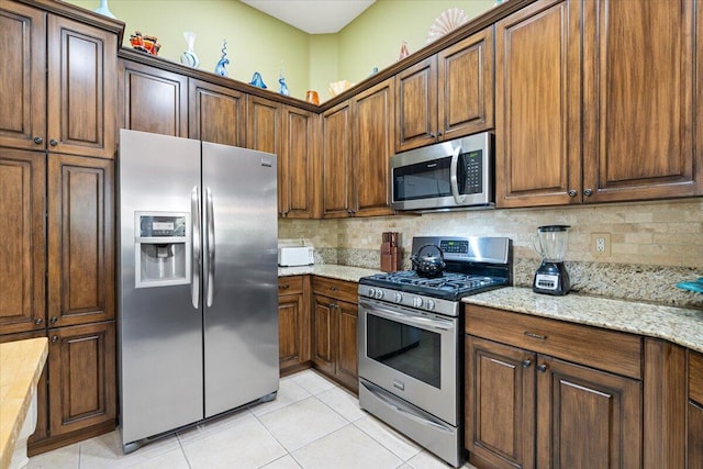 kitchen featuring decorative backsplash, appliances with stainless steel finishes, light tile patterned floors, and light stone countertops