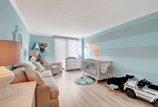 bedroom with a crib, ornamental molding, and light hardwood / wood-style flooring