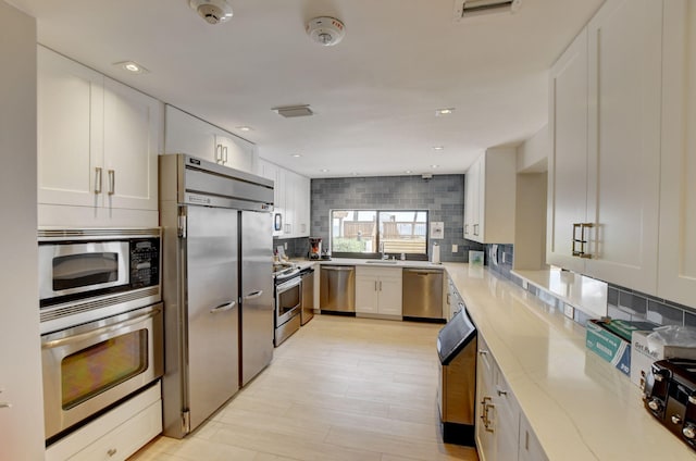 kitchen featuring built in appliances, decorative backsplash, light hardwood / wood-style floors, and white cabinetry