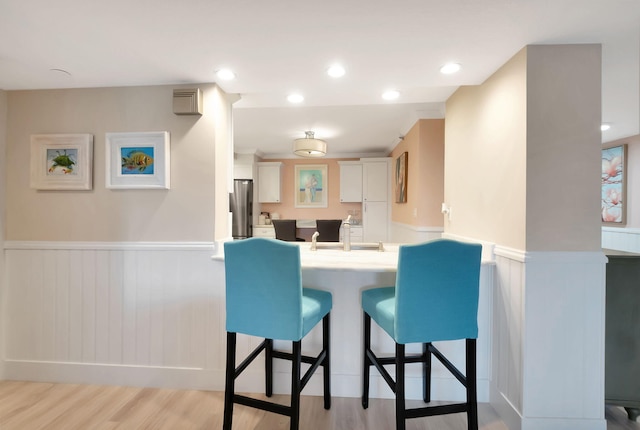 kitchen featuring white cabinetry, a kitchen breakfast bar, kitchen peninsula, stainless steel fridge, and light hardwood / wood-style floors