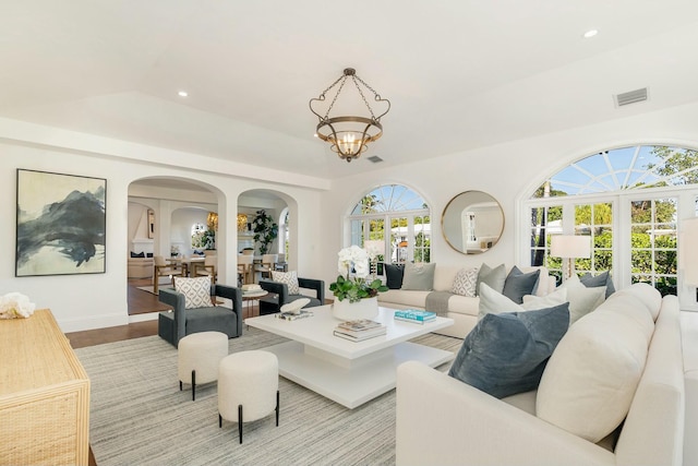 living room with an inviting chandelier, lofted ceiling, light hardwood / wood-style flooring, and french doors